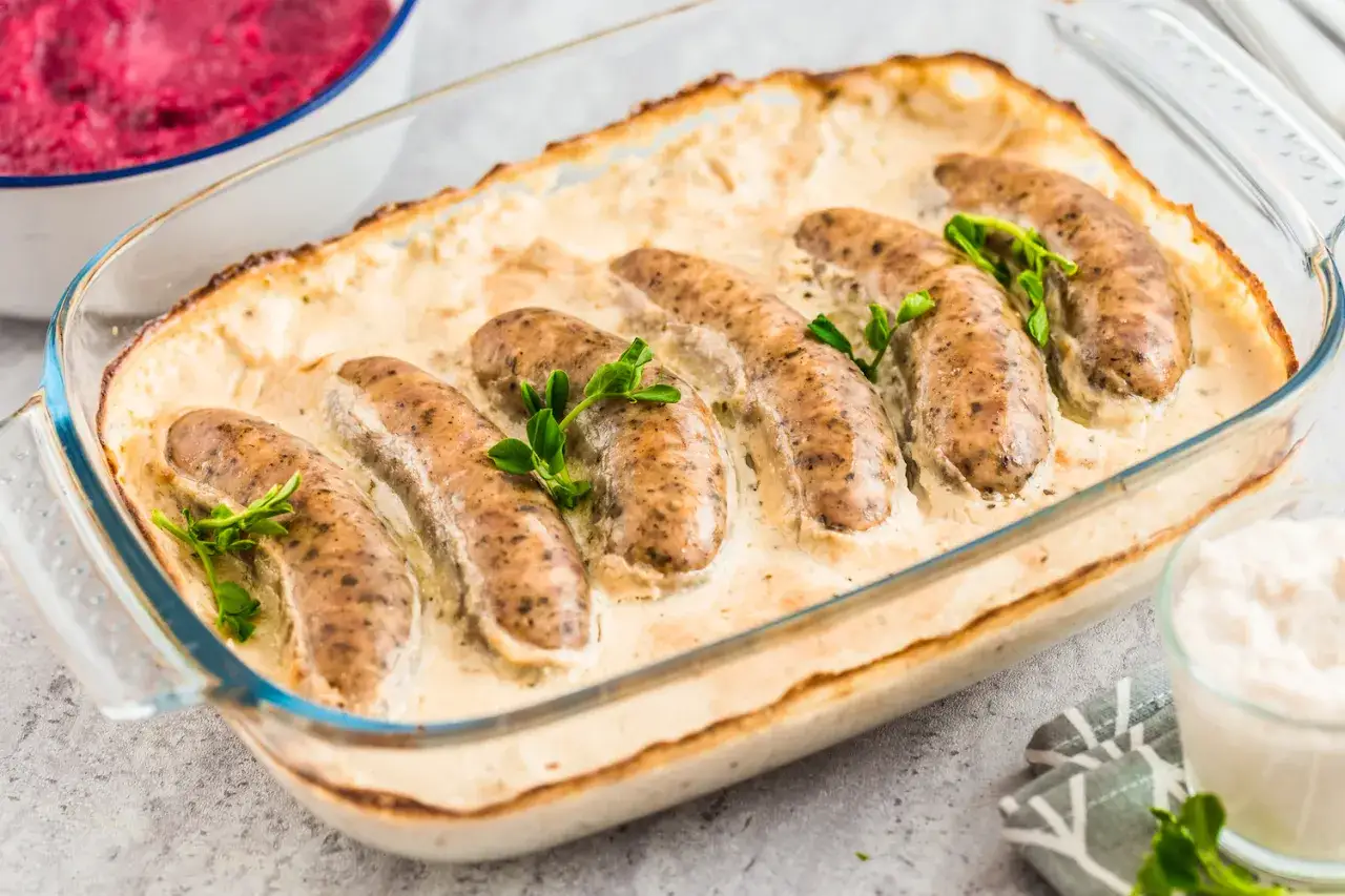 Siedem pysznych kiełbasek w kremowym sosie, zapieczonych w szklanym naczyniu. To idealna biała kiełbasa z piekarnika, podana z buraczkami.