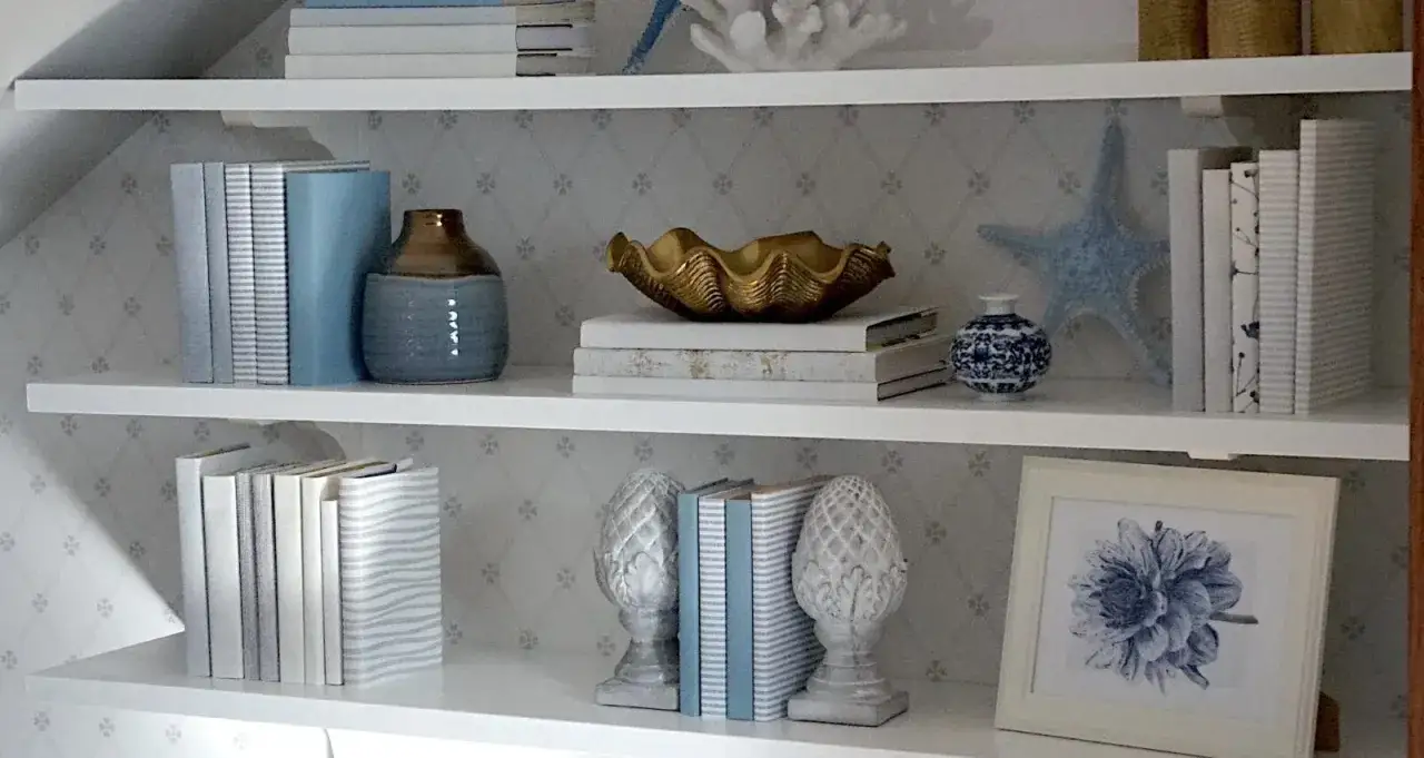 Urocze dekoracje na półki: książki, wazony, muszla i morska gwiazda tworzą nadmorski klimat.