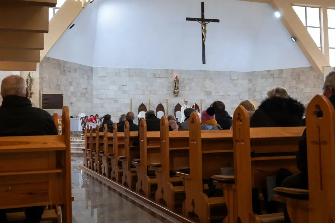 Wierni uczestniczą w liturgii Wielkiego Czwartku w kościele. Widok zza drewnianych ławek na ołtarz i krzyż.