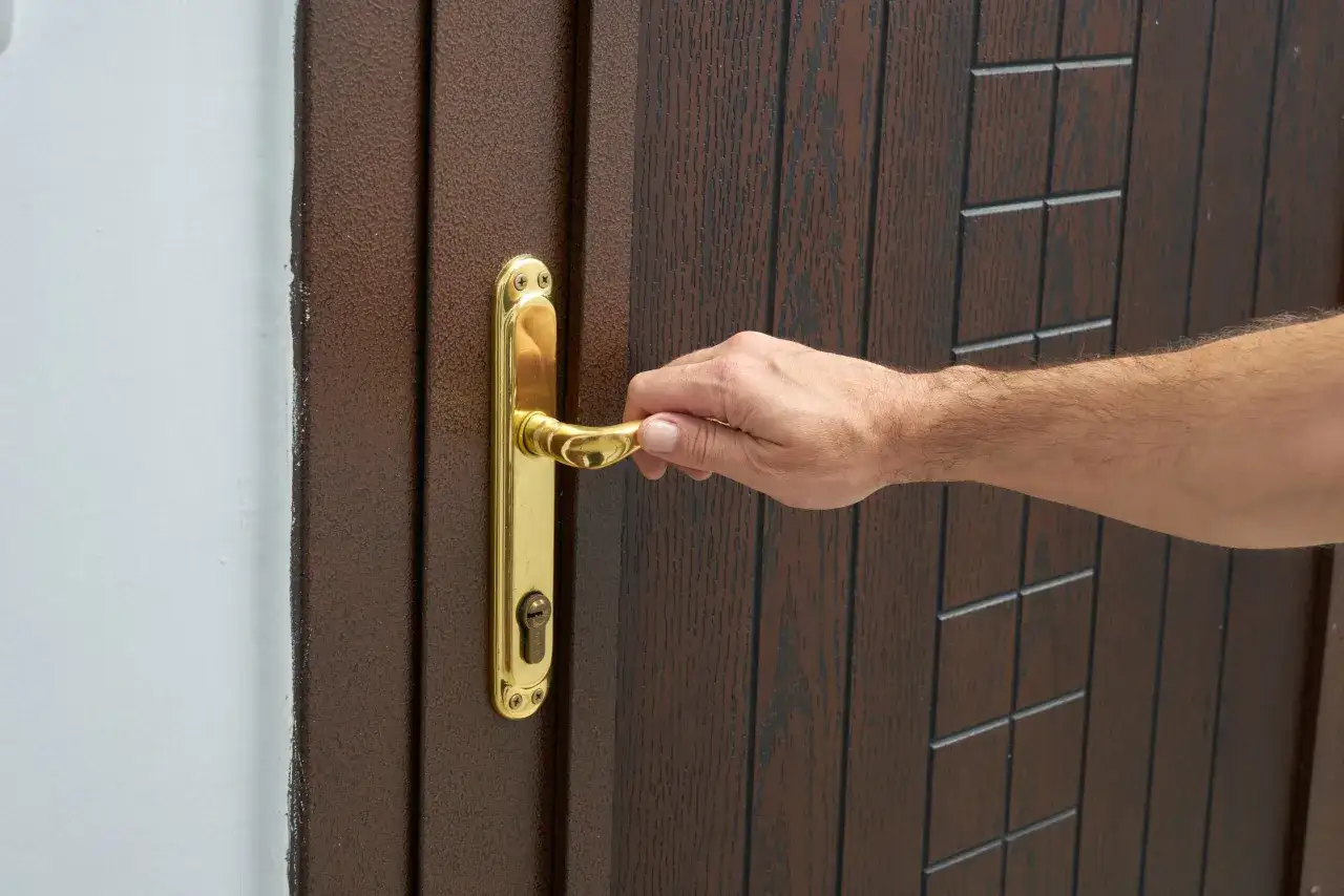 Dłoń naciska na złoty uchwyt, pokazując, jak otworzyć zamek w drzwiach pokojowych.