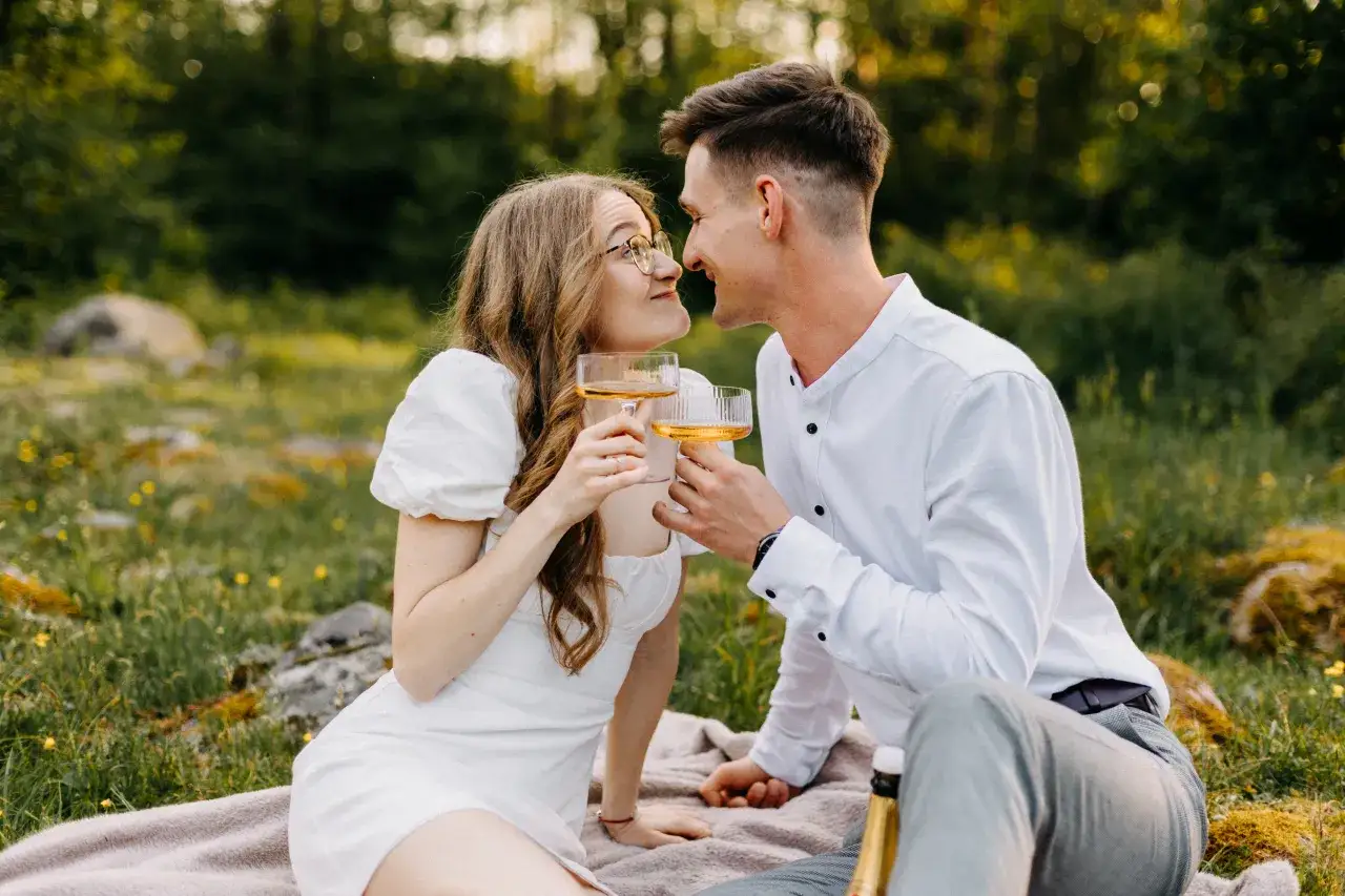 Urocza sesja zdjęciowa dla par na pikniku. Młodzi toastują winem, patrząc sobie w oczy.