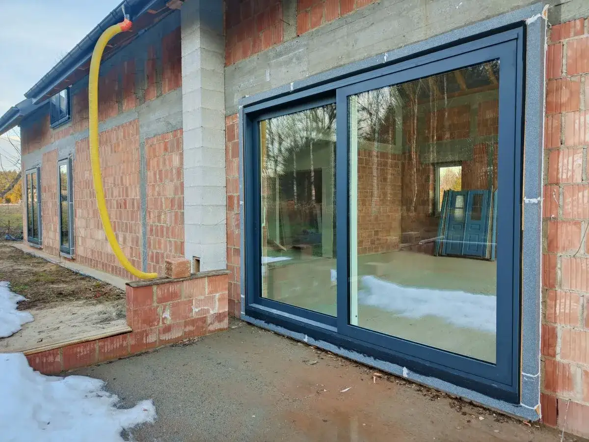 Nowe okna przesuwne w trakcie ciepłego montażu. Widać izolację i przygotowanie do wykończenia.