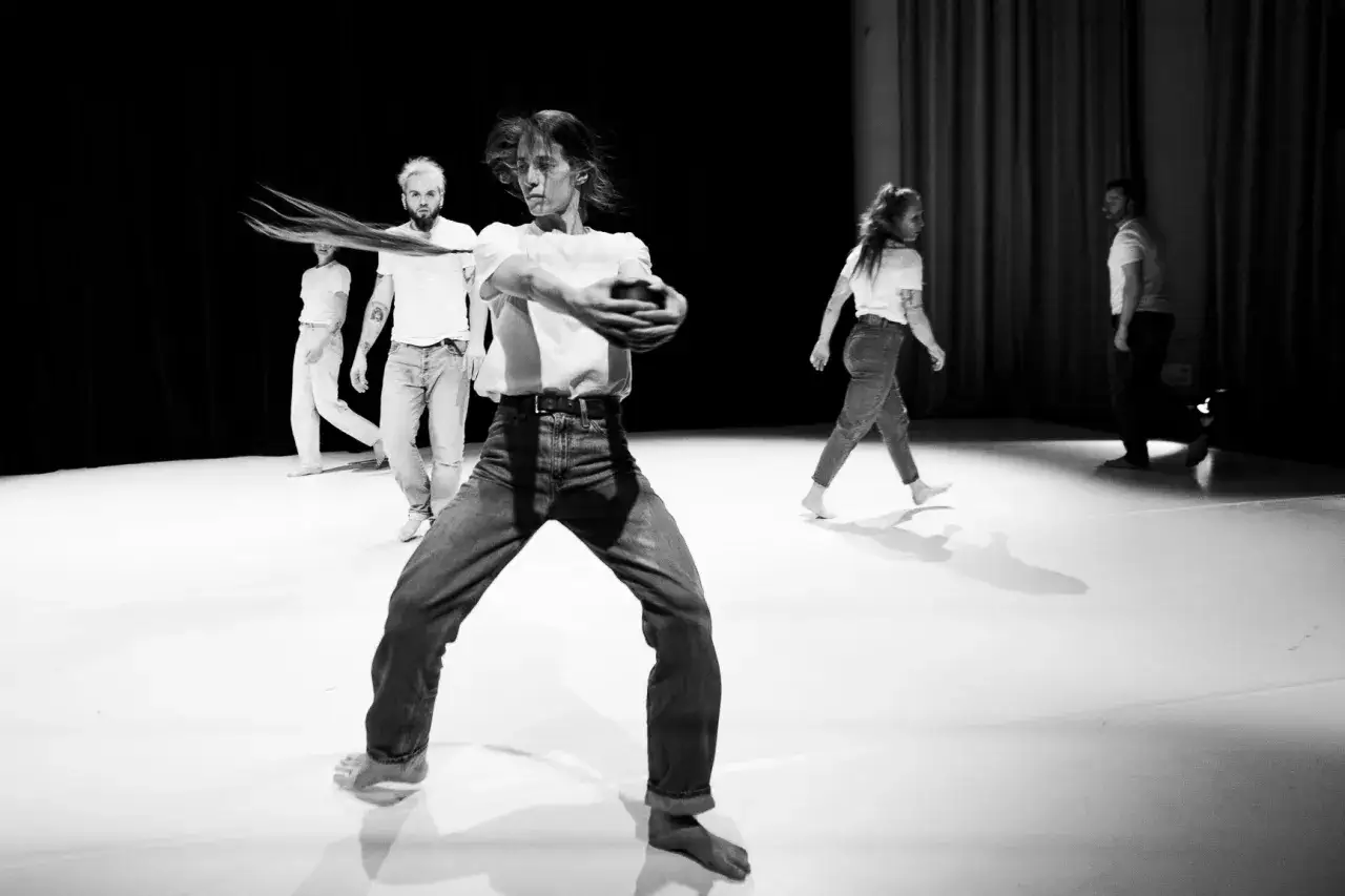 Choreograf tworzy ruch, kierując tancerzami na scenie. Widać tu grupę ludzi w ruchu, tworzących dynamiczną kompozycję.