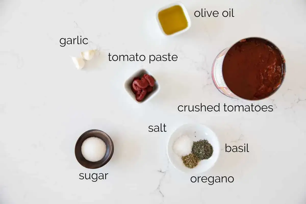 Składniki na domowy sos do pizzy: pomidory z puszki, koncentrat pomidorowy, czosnek, oliwa, s&oacute;l, cukier, bazylia i oregano.