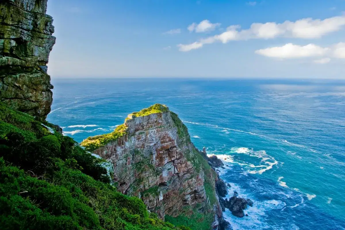 Skaliste wybrzeże RPA w pobliżu Przylądka Dobrej Nadziei, z zielonymi zboczami i turkusowym oceanem.