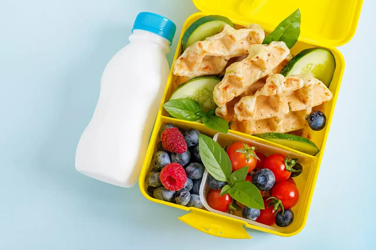 Kolorowy lunchbox z goframi, owocami i warzywami to idealna propozycja, co na drugie śniadanie dla rocznego dziecka. Butelka z napojem uzupełnia zestaw.