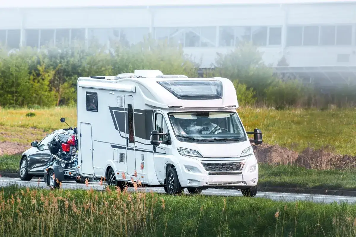 Biały kamper z przyczepą i motocyklem. Zastanawiasz się, ile kosztuje kamper?