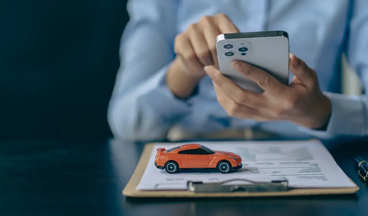 Pomarańczowy model samochodu na dokumentach, osoba wybiera ubezpieczenie nowego samochodu z salonu przez telefon.