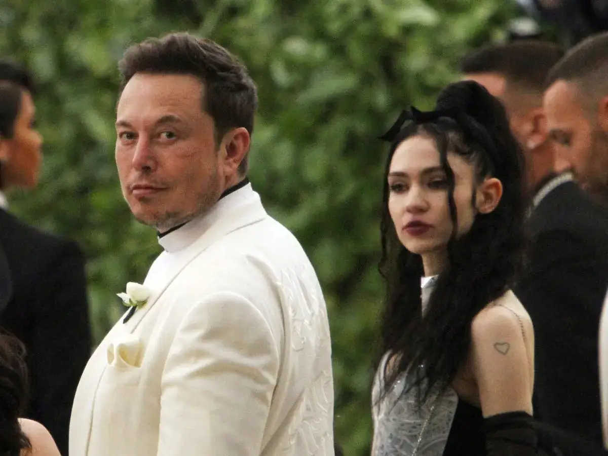 Elon Musk w białym garniturze obok Grimes, która ma na sobie błyszczącą suknię.