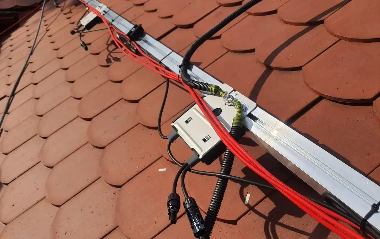 Instalacja fotowoltaiczna na dachu. Widać przewody, skrzynkę przyłączeniową i szynę montażową. Pytanie, czy uziemienie można podłączyć do minusa, jest kluczowe dla bezpieczeństwa.