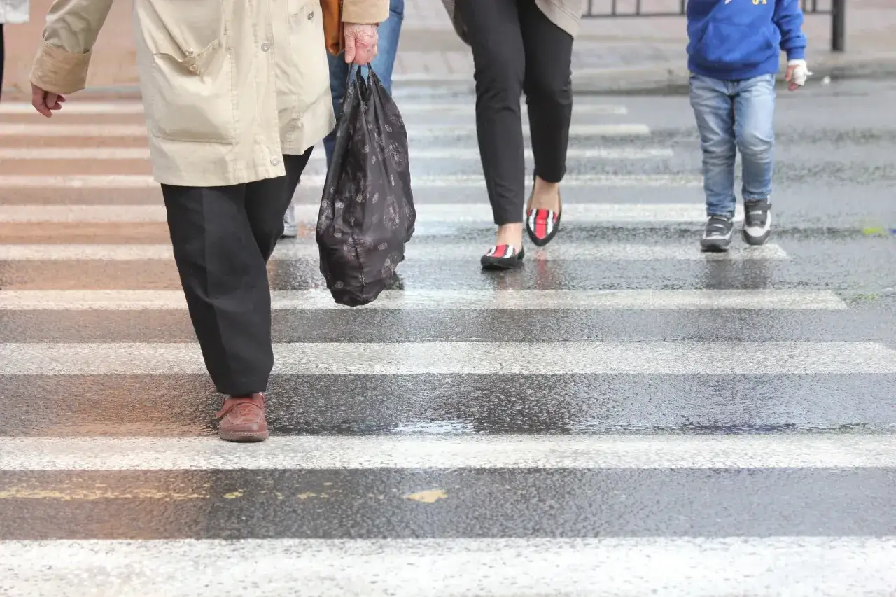 Ludzie przechodzą przez mokre pasy. Warto pamiętać o bezpieczeństwie, by uniknąć wypadku i konieczności dochodzenia odszkodowania za potrącenie na pasach.