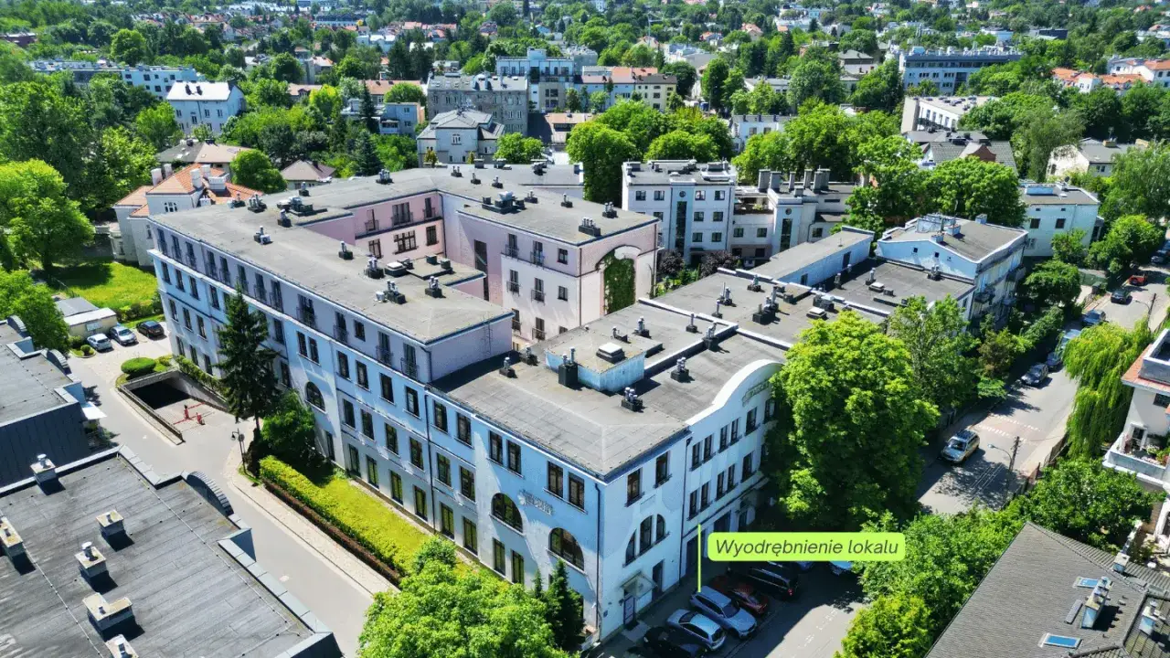 Widok z lotu ptaka na budynek mieszkalny, który stanowi odrębną nieruchomość. Widać otoczenie z drzewami i innymi budynkami.