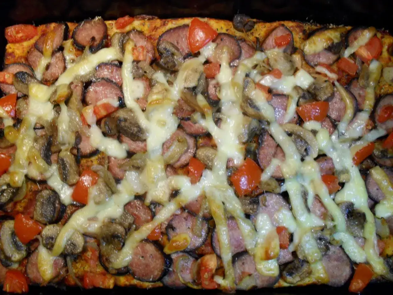 Pyszna pizza z kiełbasą, pieczarkami i pomidorami, obficie posypana ciągnącym się serem.