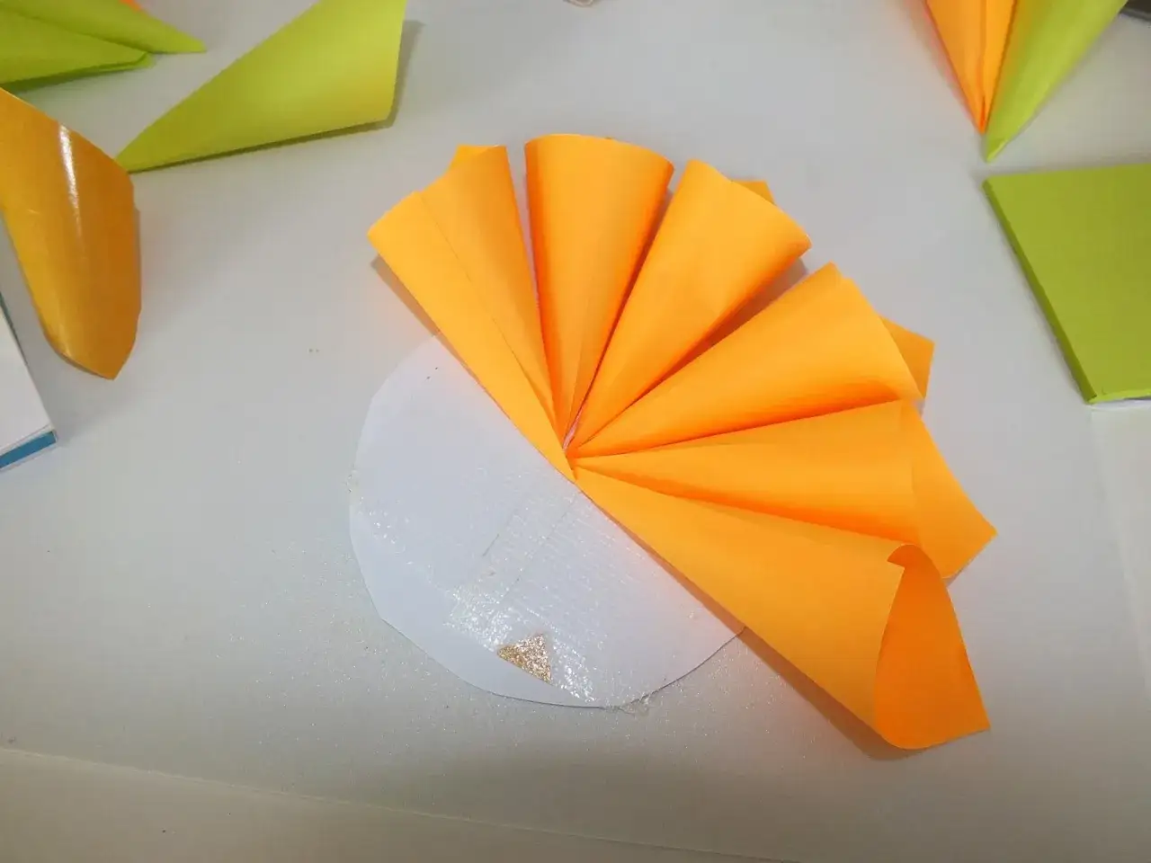 Jak zrobić kwiaty z papieru 3d? Pomarańczowe stożki z papieru tworzą efektowny kwiat, przyklejone do białej podstawy.
