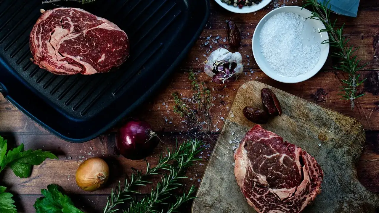 Dwa soczyste steki wołowe, czosnek, cebula, zioła i s&oacute;l &ndash; wszystko gotowe do przygotowania pysznej zalewy do mięsa.