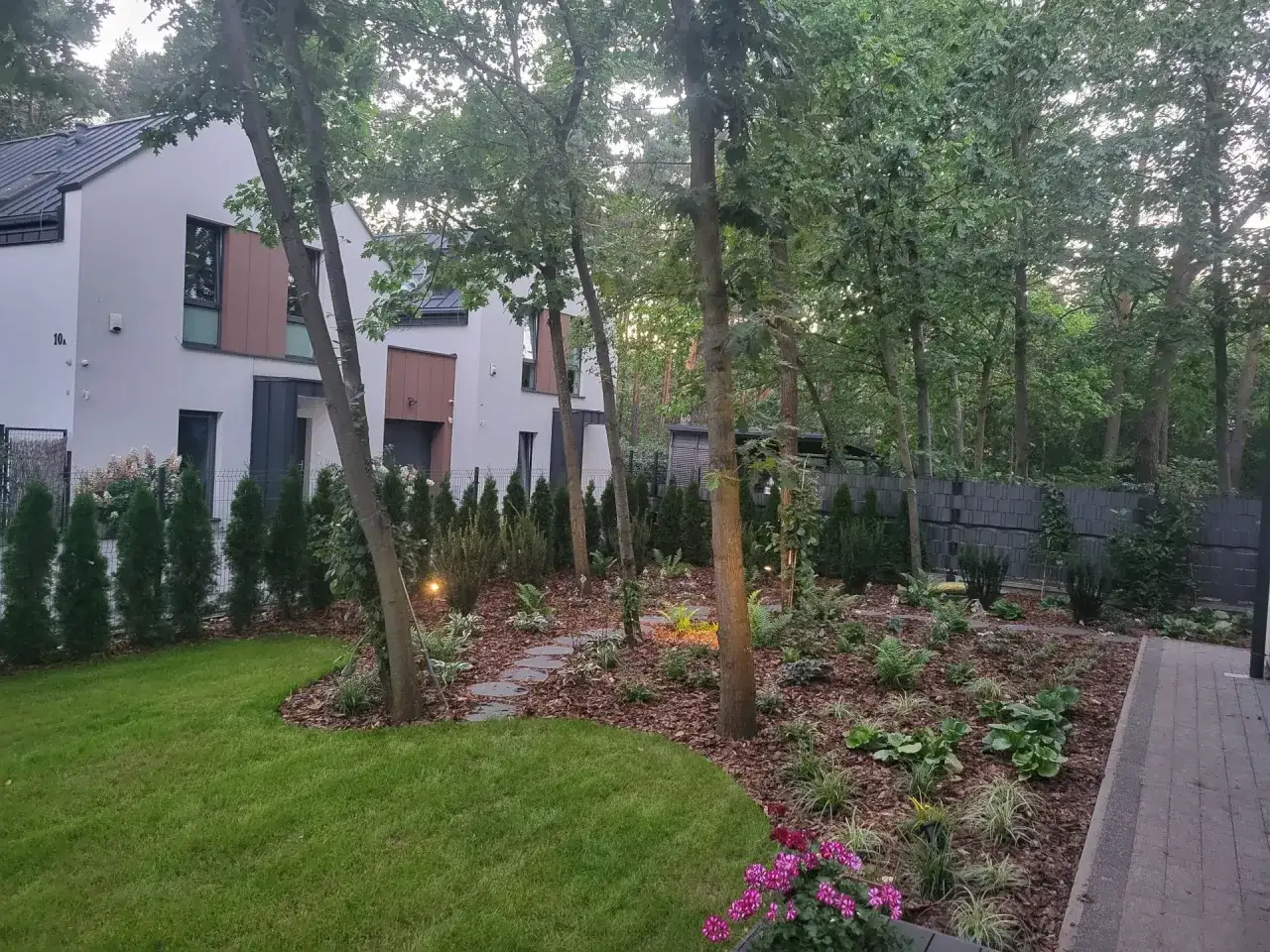 Nowoczesne ogrody przydomowe z zadbanym trawnikiem, ścieżką z kamieni i bujną roślinnością.