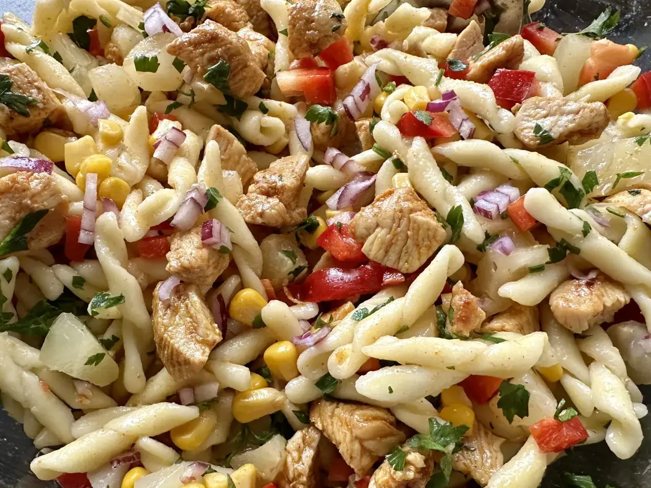 Pyszna sałatka makaron z kurczakiem, kukurydzą, czerwoną cebulą i papryką, posypana natką pietruszki.