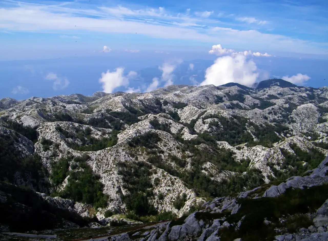 G&oacute;rzysty krajobraz Chorwacji z kamienistymi zboczami i zielonymi dolinami. W oddali widać morze i chmury. To widok z najwyższego szczytu w Chorwacji.