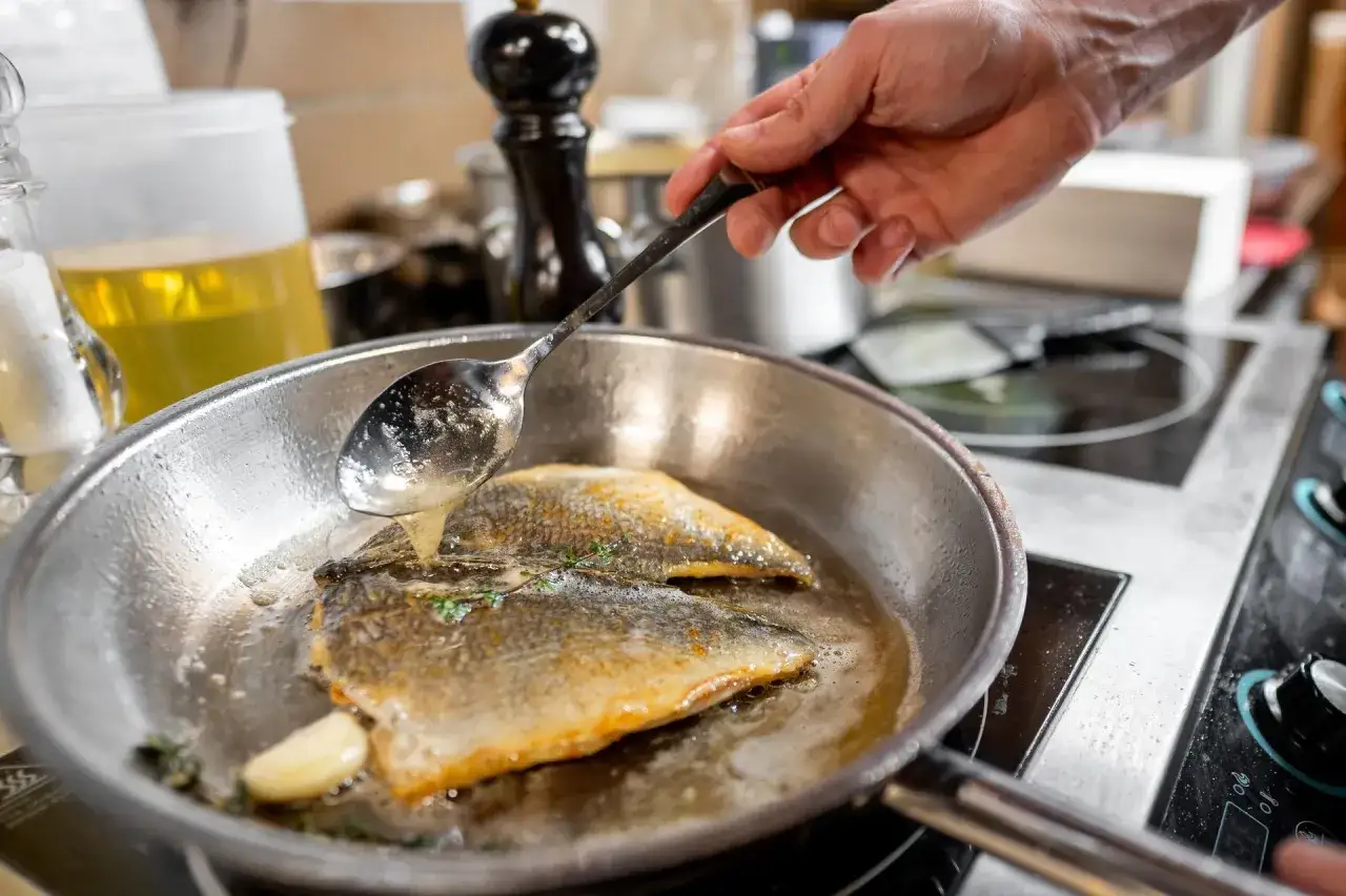 Ręka polewa rybę na patelni, pokazując, jak smażyć ryby mrożone.