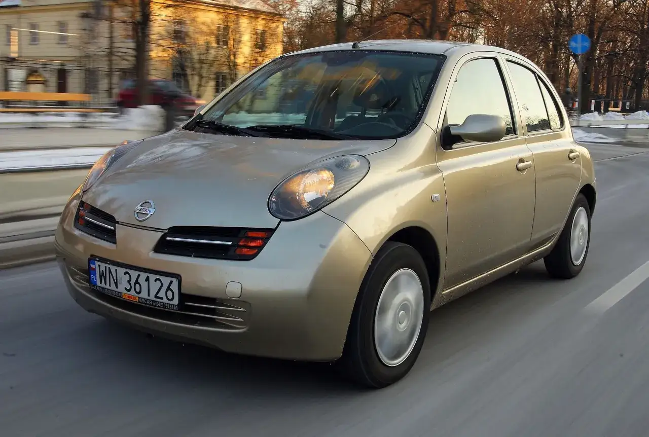 Złoty Nissan Micra, małe auto z automatyczną skrzynią biegów do 10 tys. zł, jedzie po drodze.