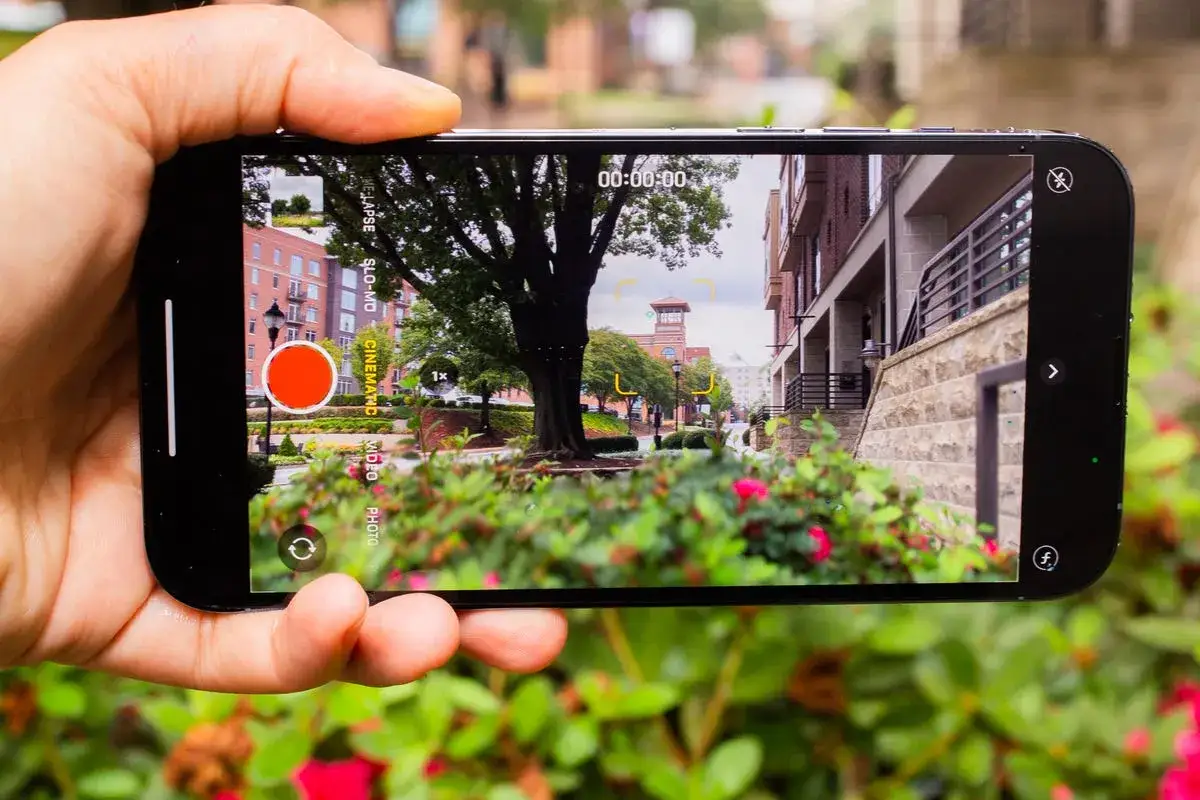 Dłoń trzyma iPhone 13 Pro, nagrywając film z miejskim krajobrazem. Widoczny interfejs kamery.