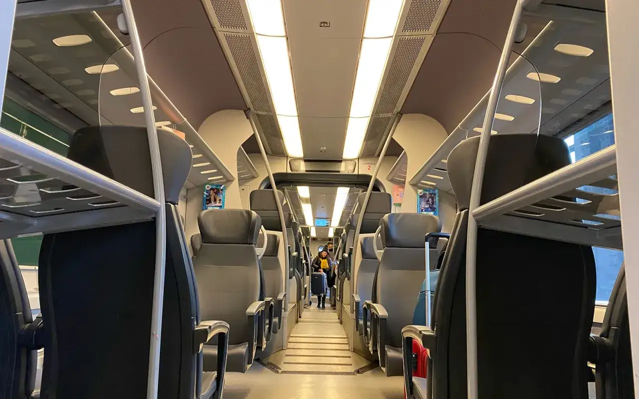 Wnętrze pociągu do portu lotniczego Mediolan Malpensa. Pasażerowie z bagażami zajmują miejsca.