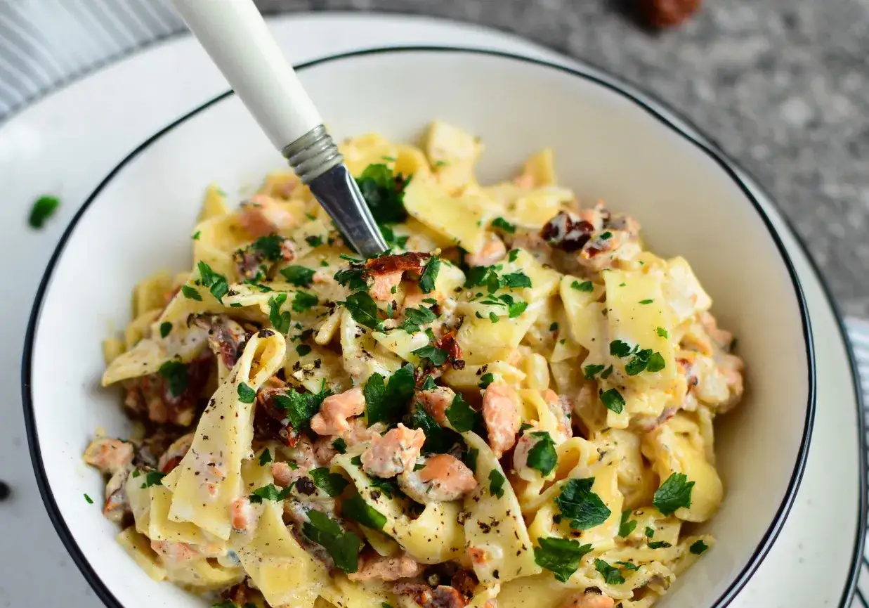 Pyszny makaron z łososiem i suszonymi pomidorami, posypany świeżą natką pietruszki. Idealny na szybki obiad.