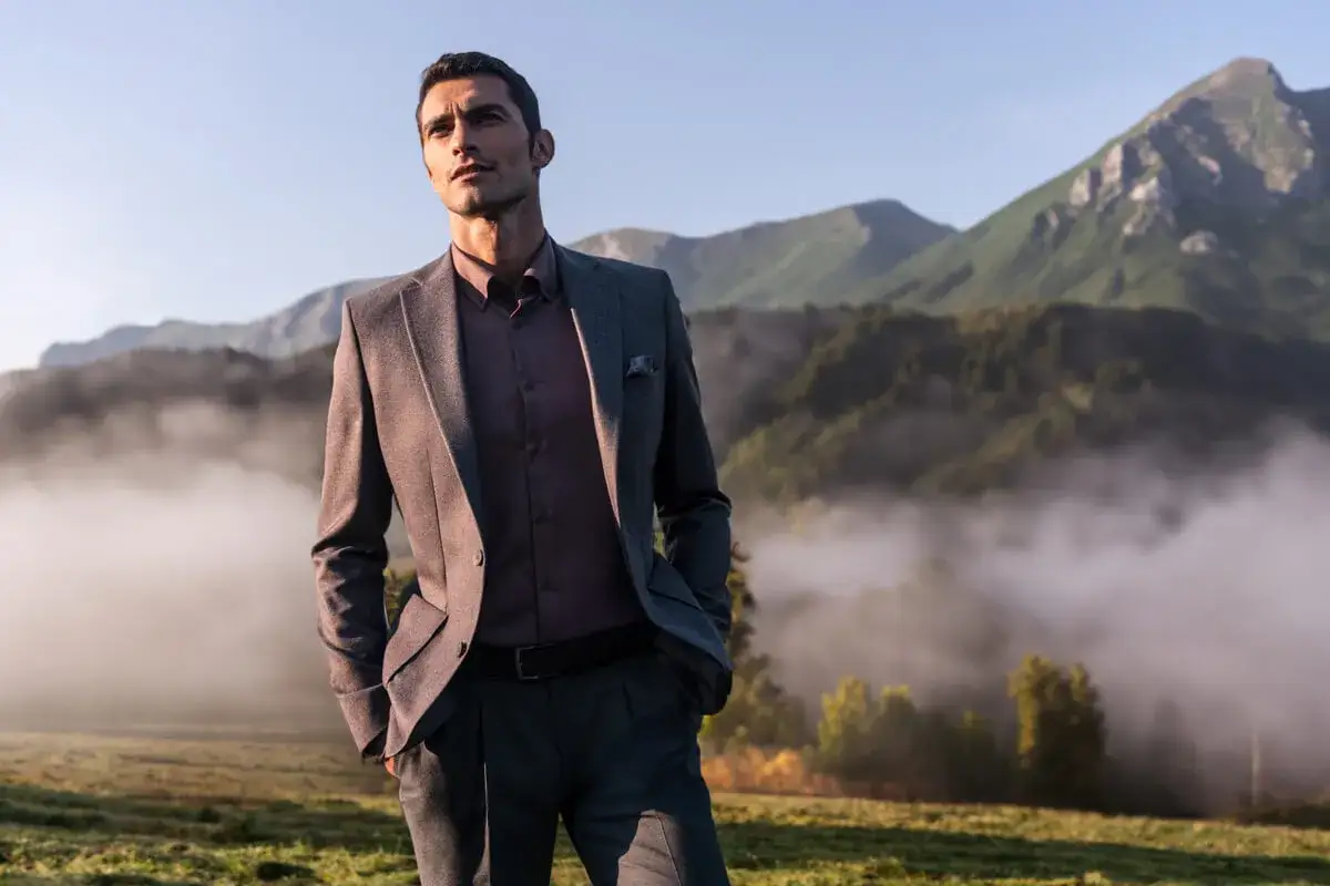Przystojny facet w eleganckim garniturze, z rękami w kieszeniach, podziwia g&oacute;rski krajobraz o poranku.