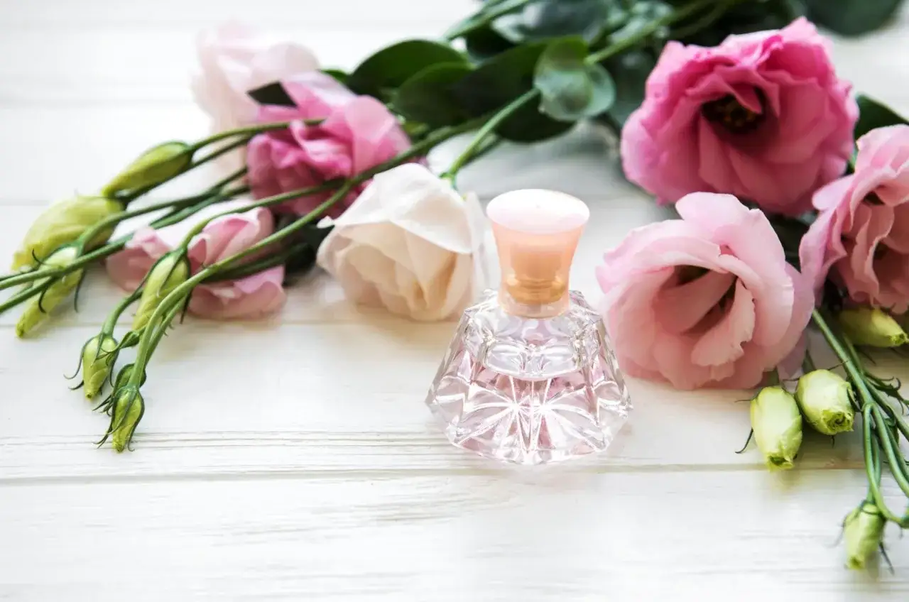 Elegancka buteleczka perfum wśród różowych kwiatów i pąków. Inspiracja do tego, jak zrobić perfumy z płatków róż.