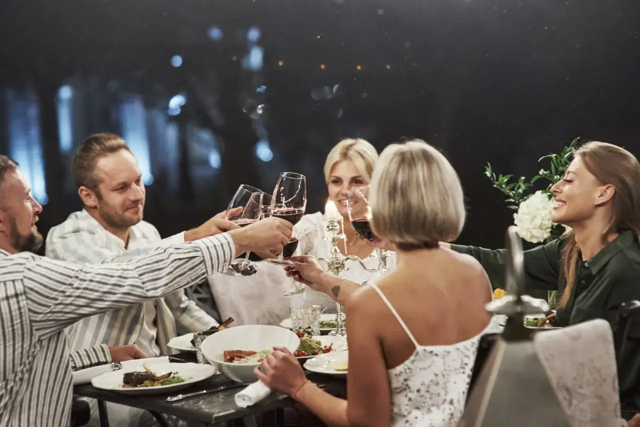 Grupa przyjaciół wznosi toast kieliszkami wina podczas eleganckiej kolacji. Zastanawiasz się, ile kosztuje wesele na 50 osób?