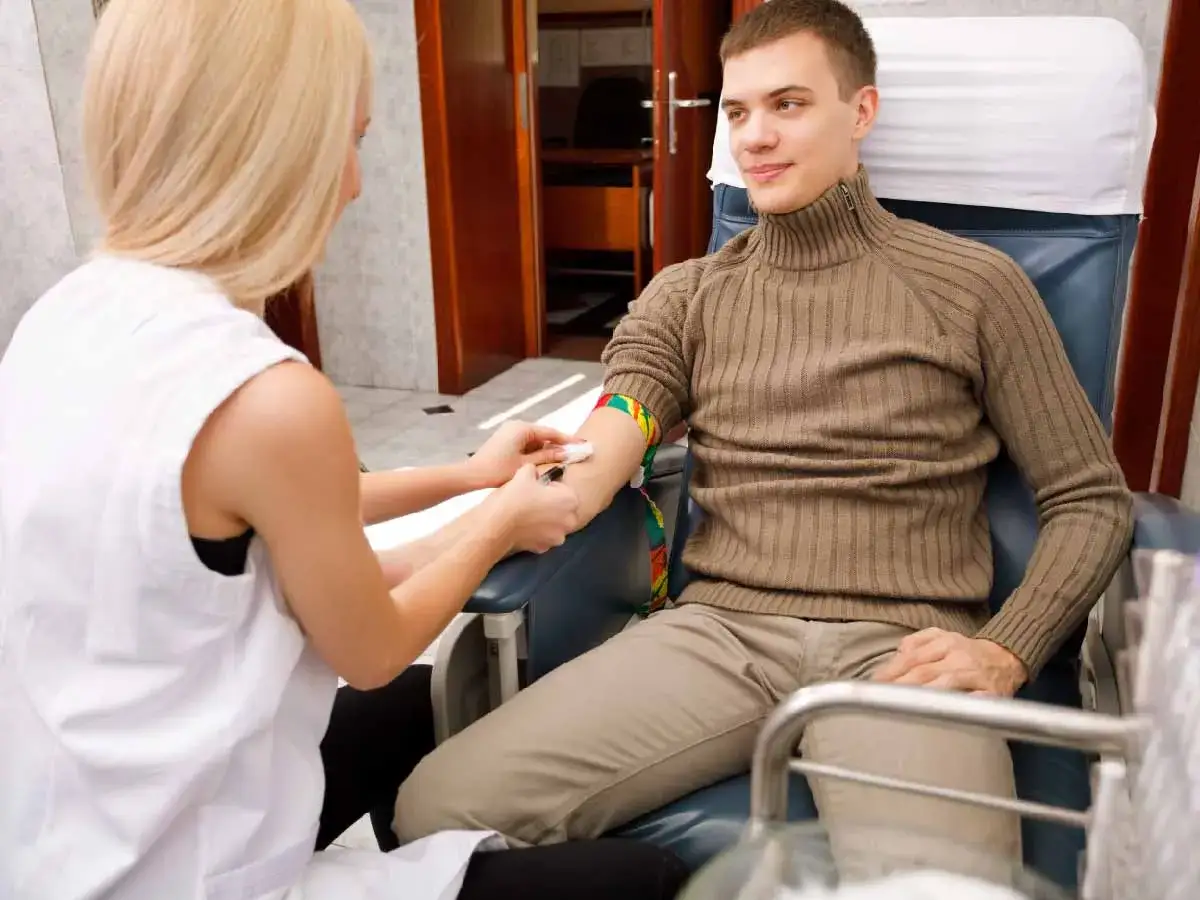 Młody mężczyzna siedzi w fotelu, pielęgniarka pobiera mu krew. Może to być związane z nagłą nietolerancją alkoholu.