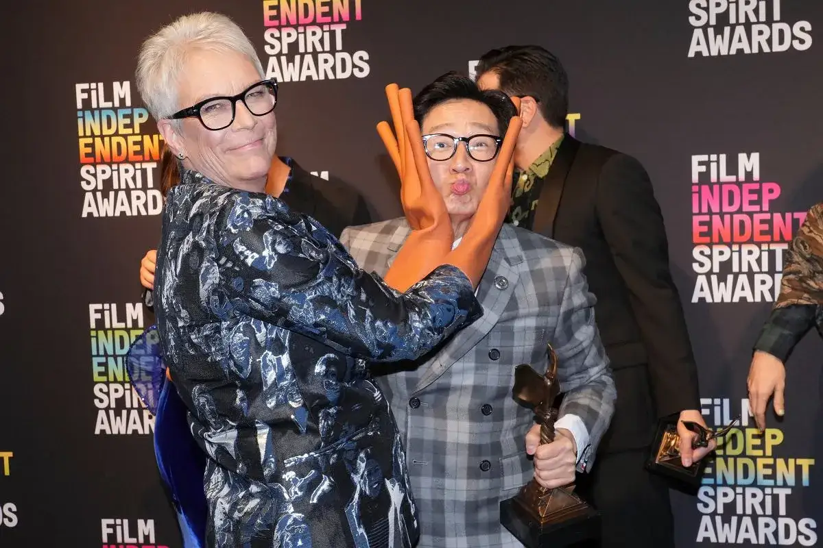 Jamie Lee Curtis robi śmieszną minę Ke Huy Quanowi, który trzyma statuetkę. To scena z gali wręczenia nagród, która przypomina klimat filmu 