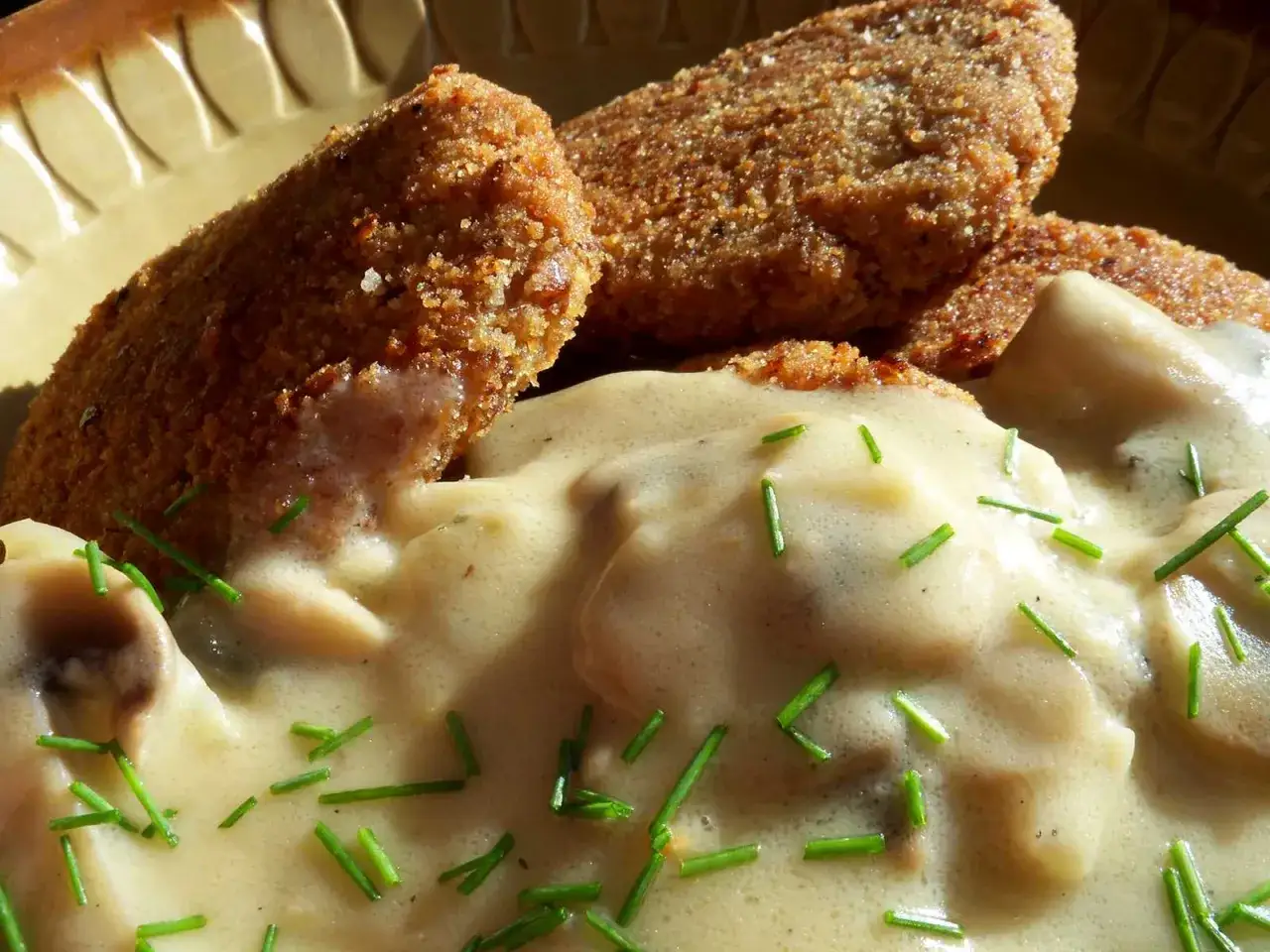 Chrupiące kotleciki w kremowym sosie pieczarkowym, posypane szczypiorkiem. Pyszne danie, które aż prosi się o dokładkę.