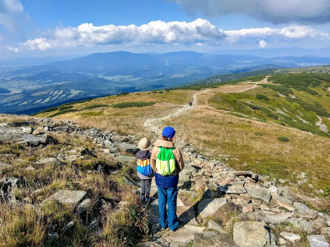 Dzieci idą kamienistym szlakiem na Babią Górę. W tle rozciąga się malowniczy krajobraz Beskidów.
