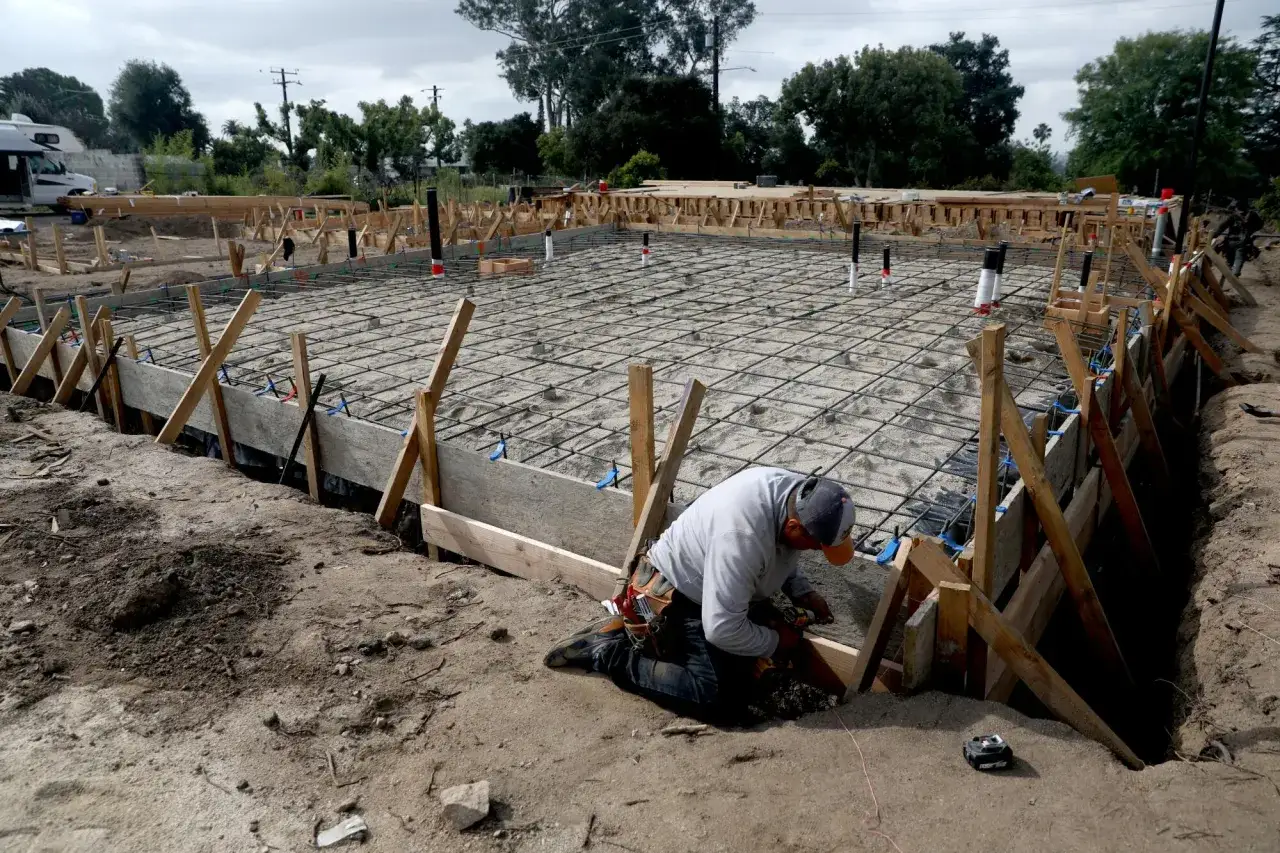 Budowa fundamentu pod pompę ciepła. Robotnik pracuje przy zbrojeniu i deskowaniu.