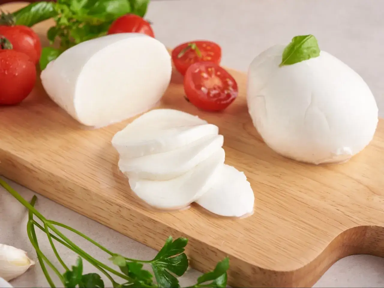 Świeża mozzarella, pomidorki i bazylia na desce. Czy mozzarella jest zdrowa? Tak, w umiarkowanych ilościach dostarcza białka i wapnia.