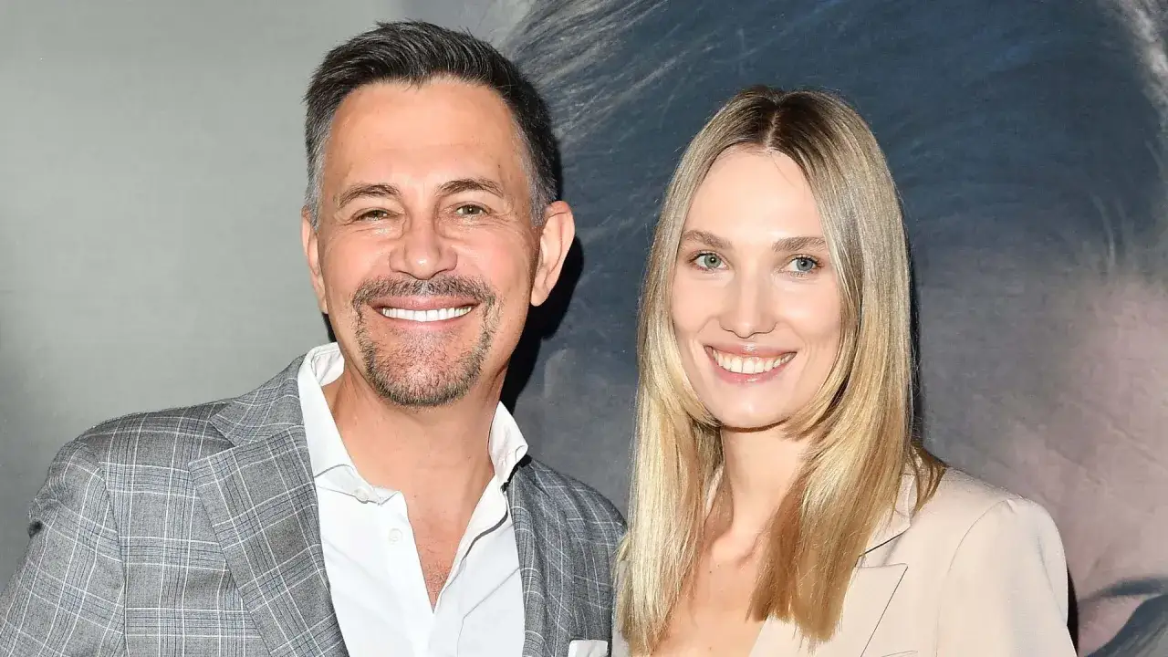 Krzysztof Ibisz z żoną, Anną, uśmiechnięci na tle plakatu. Ich szczęście to prawdziwy majątek.