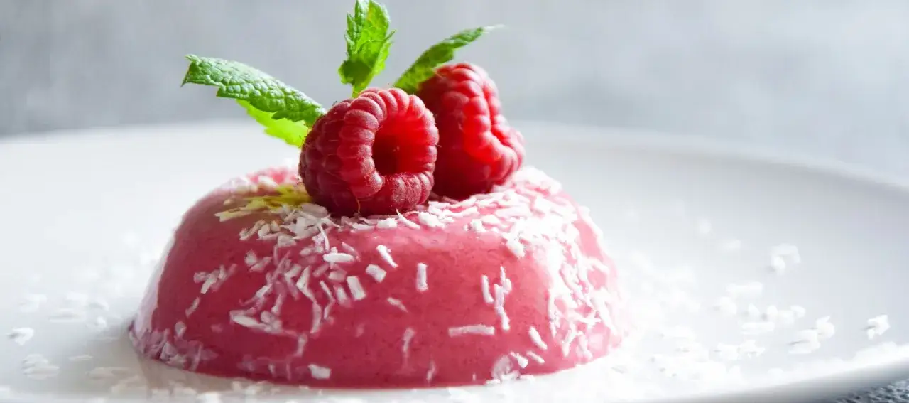 Malinowa Panna Cotta przepis. Delikatny deser z malinami i miętą, posypany wiórkami kokosowymi.