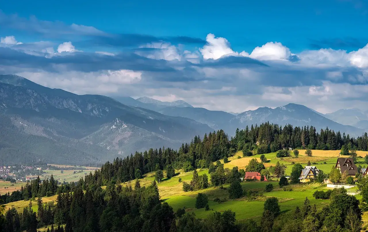 Widok na najwyższe pasma górskie w Polsce, Tatry, z zielonymi dolinami, lasami i kilkoma domami.