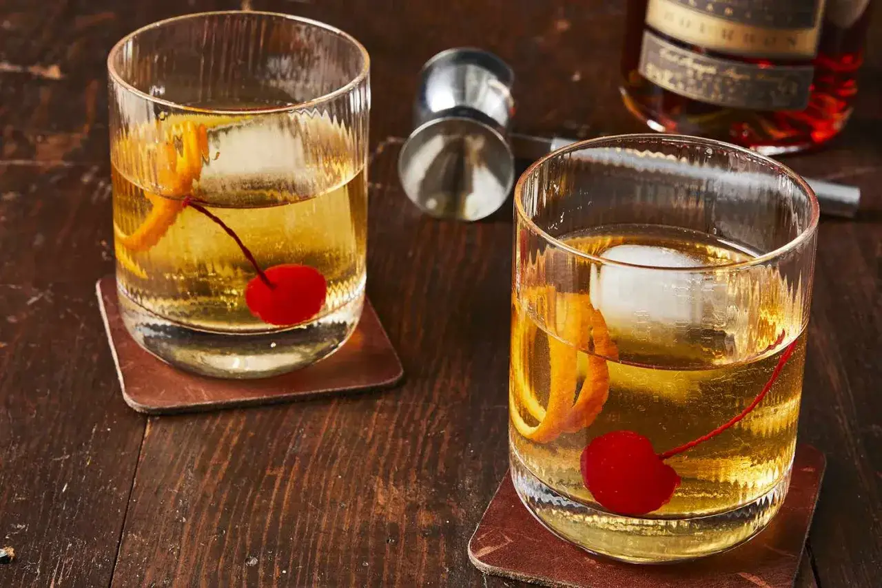 Dwa klasyczne drinki whisky old fashioned z wiśnią i skórką pomarańczy na drewnianym stole.