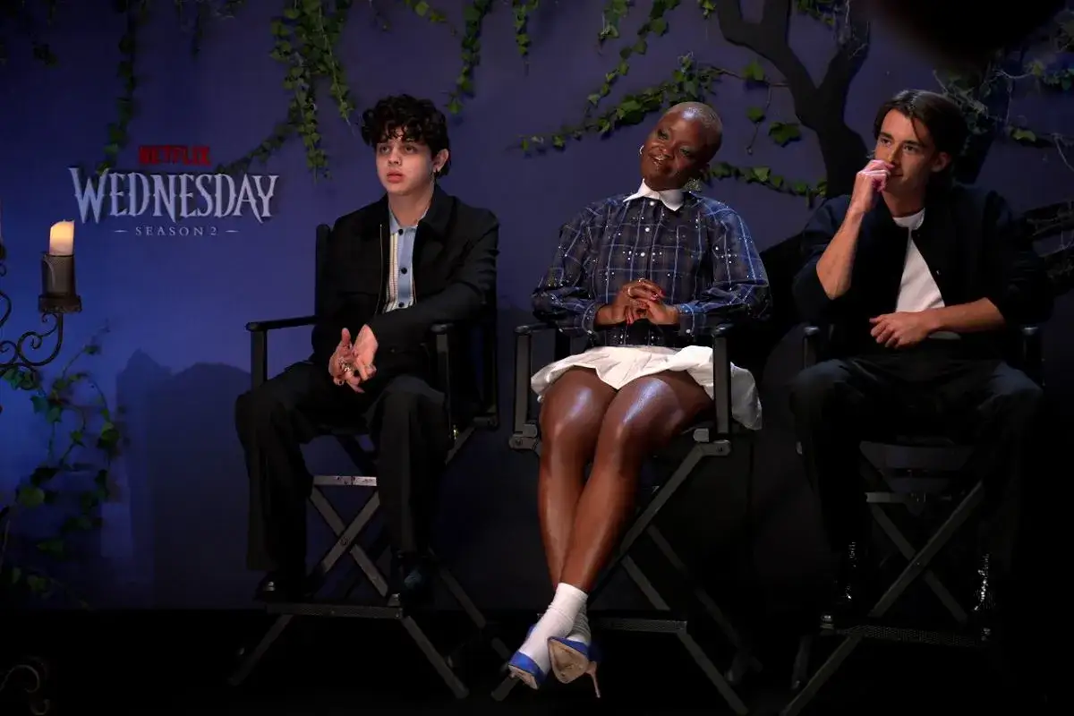 Trzech aktorów siedzi na krzesłach przed plakatem 