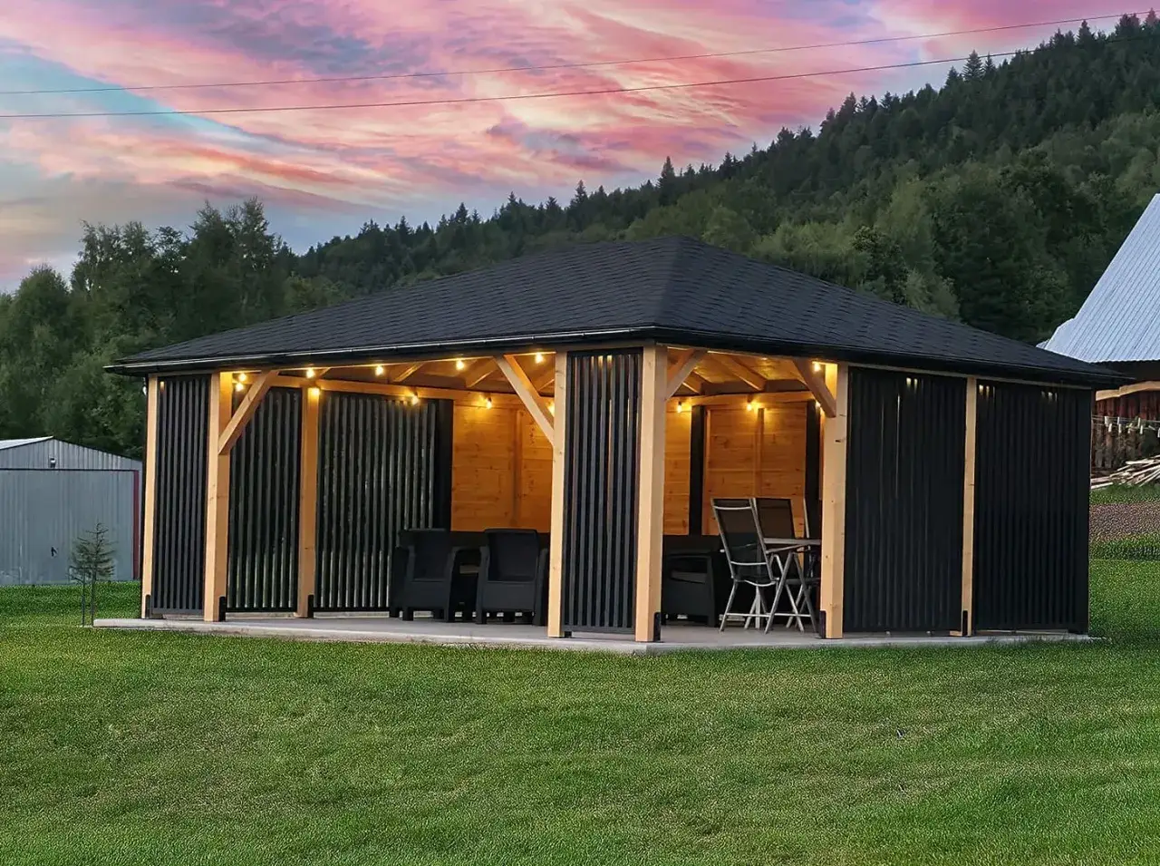Nowoczesna altana na działce z oświetleniem i meblami, otoczona zieloną trawą i lasem.