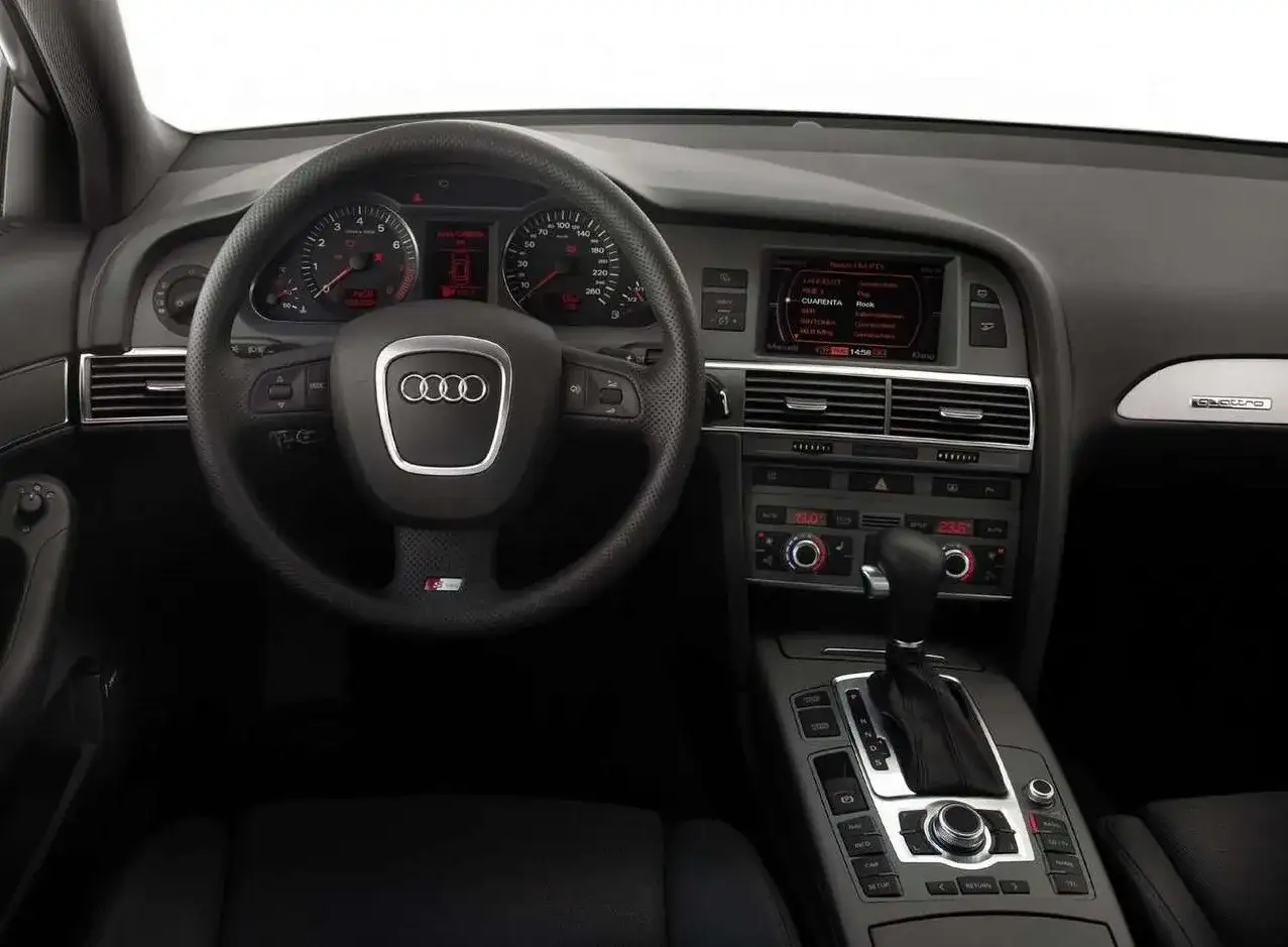 Wnętrze Audi A6 C6: kierownica, deska rozdzielcza z ekranem MMI, dźwignia zmiany biegów i przyciski konsoli środkowej.