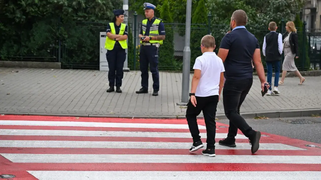Dziecko idzie do szkoły z tatą, a policja pilnuje przejścia. Od ilu lat dziecko może samo chodzić do szkoły? To zależy od wielu czynników.
