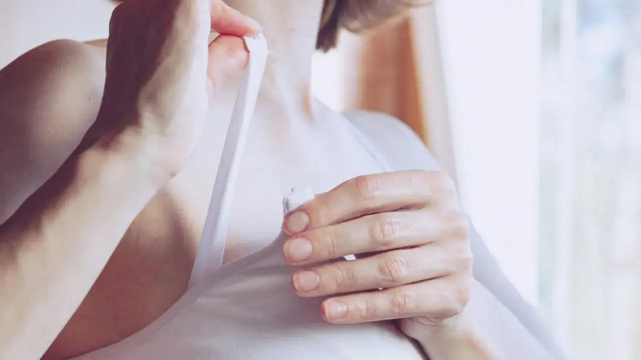 Delikatne dłonie kobiety poprawiające ramiączko biustonosza, symboliczny moment, kiedy zanika pokarm w piersiach.