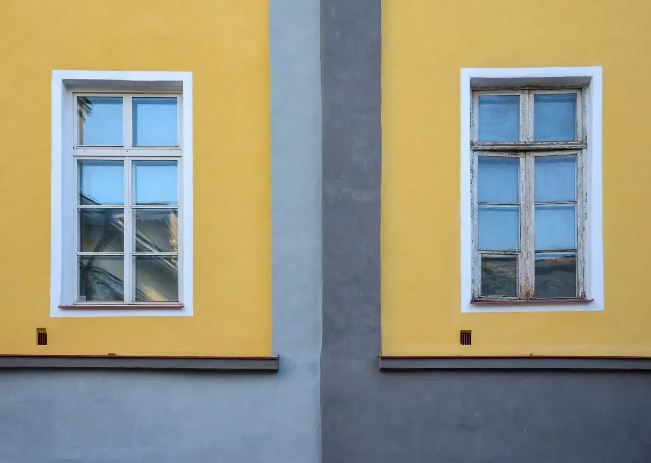 Dwa okna drewniane na ż&oacute;łtej ścianie, jedno odnowione, drugie czekające na renowację.
