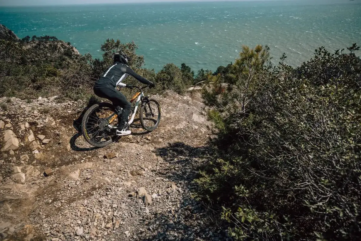 Kolarz zjeżdża po kamienistym szlaku nad morzem, czując adrenalinę wyścigu kolarskiego we Włoszech.