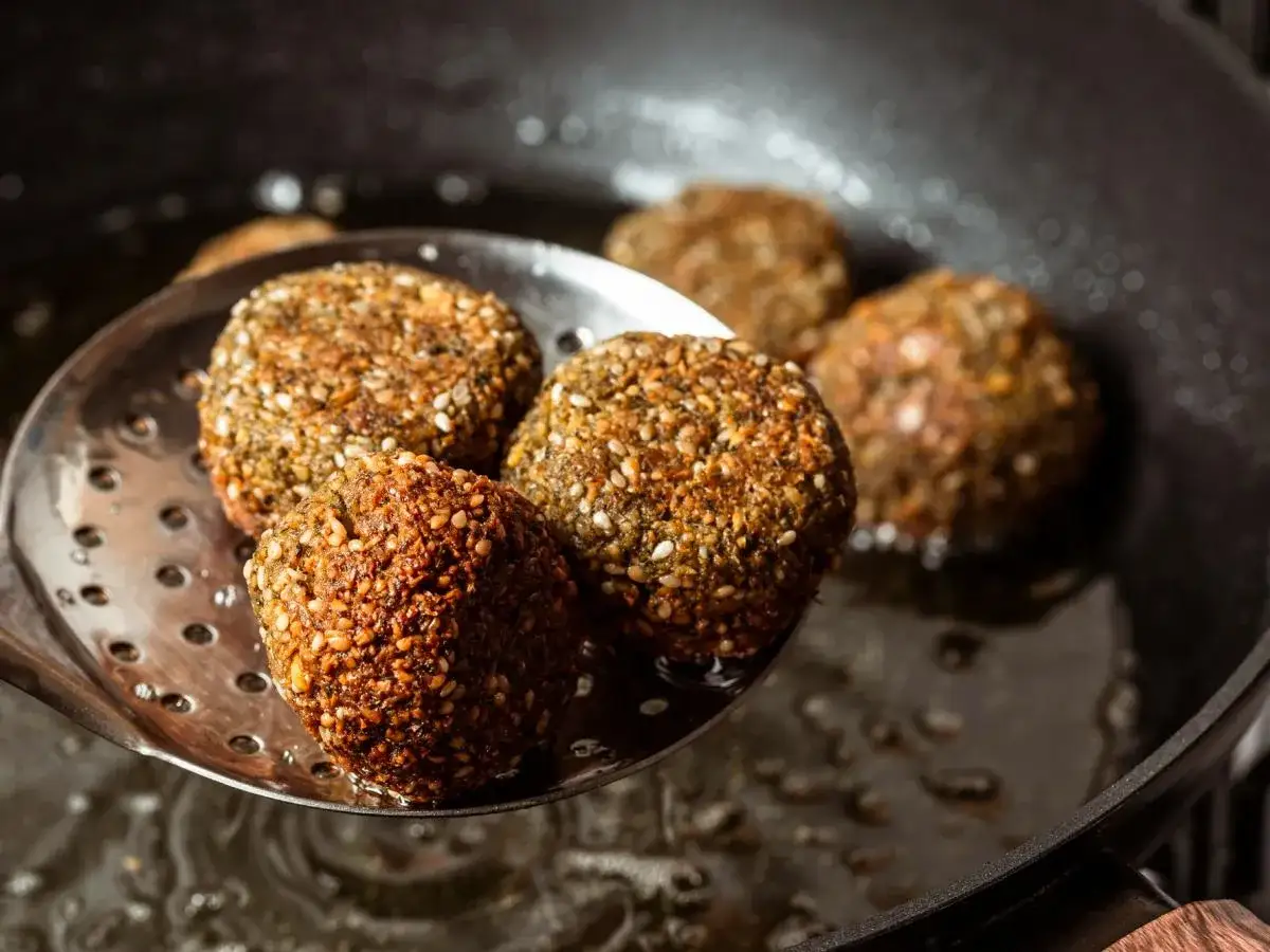 Falafel kontra kotlety sojowe: złociste kulki falafela wyjmowane z gorącego oleju, gotowe do podania.