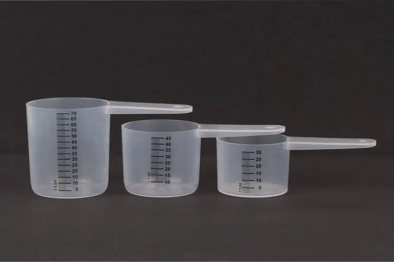 Trzy plastikowe miarki z podziałką. Największa ma oznaczenia do 70 ml, średnia do 45 ml, a najmniejsza do 30 ml. Zastanawiasz się, ile ml ma jedna łyżeczka?