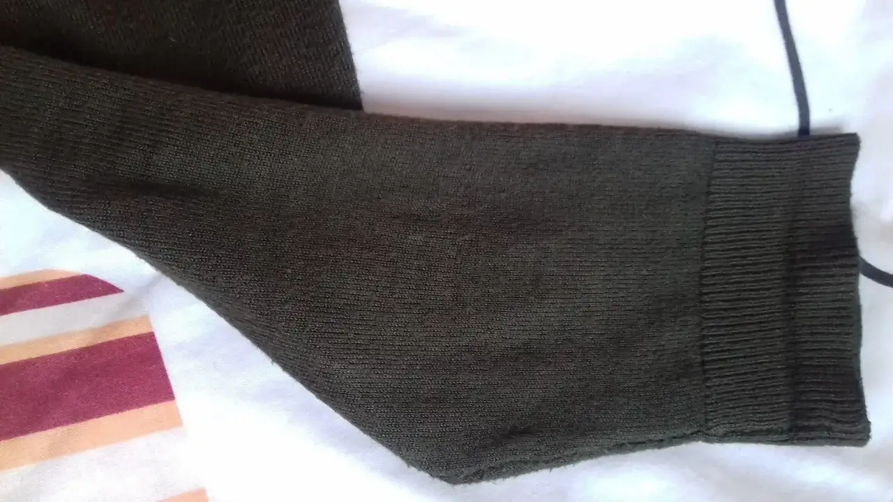 Zbliżenie na ciemnozielony rękaw swetra, pokazujące jego fakturę i ściągacz. To może być odpowiedź na pytanie, dlaczego swetry się mechacą.